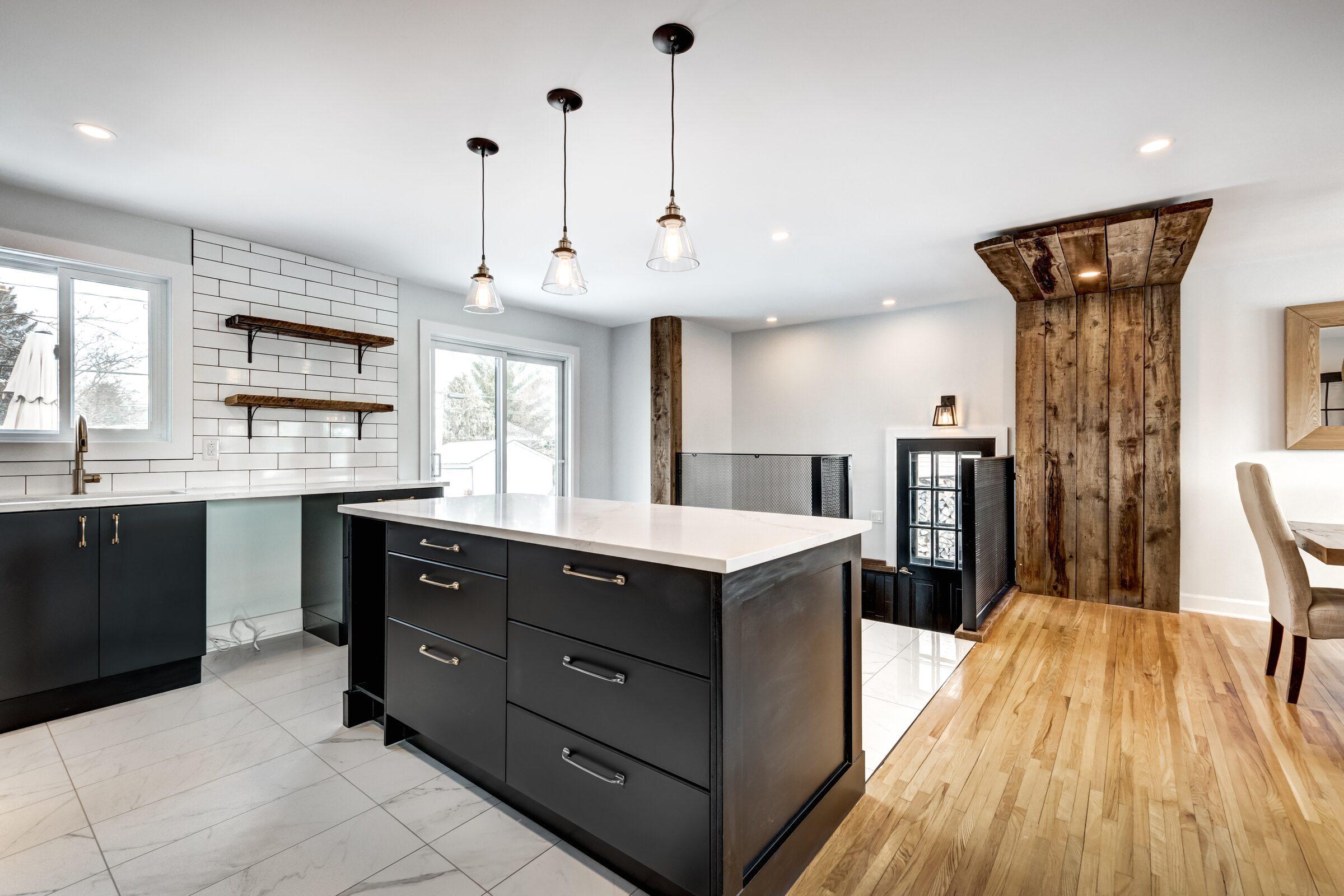 Kitchen with a black island under a white countertop, three glass pendant lights, white subway tile with open wood shelves and a rustic wood-plank wall panel