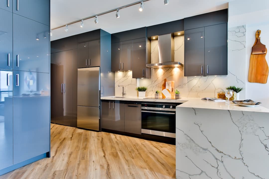 Modern kitchen with glossy grey flat-panel cabinets, stainless steel appliances, a marble-look backsplash and a waterfall-edge marble-look peninsula