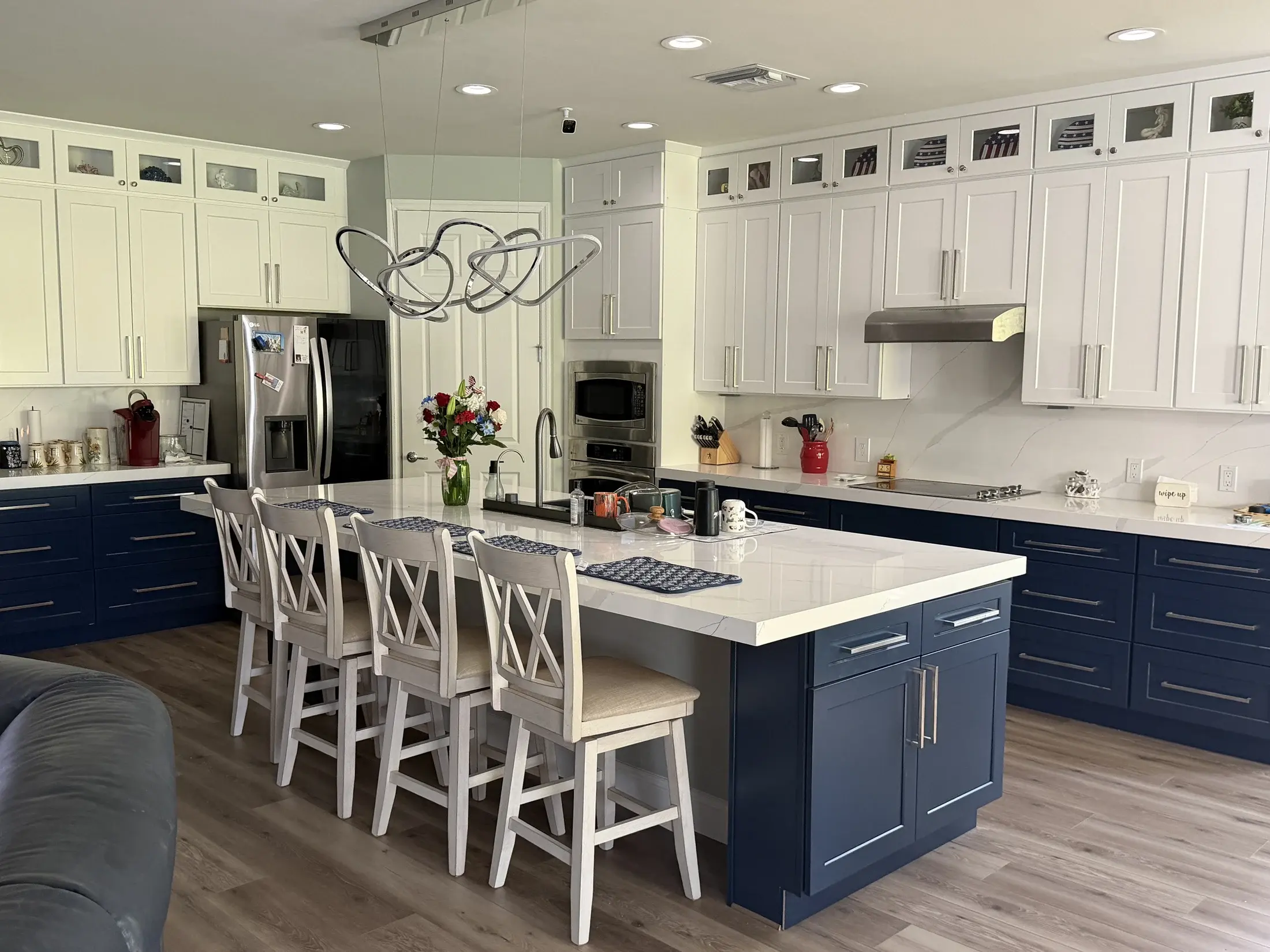 Collaborative Construction’s completed kitchen with white upper cabinets, navy lower cabinets, a quartz island and four cross-back stools